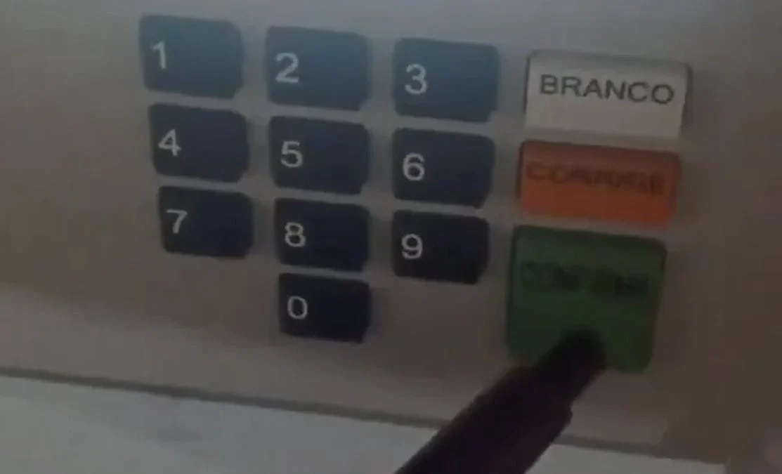 Eleitor registra voto em Flávio Bolsonaro enquanto segura arma dentro da cabine
